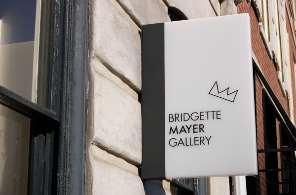 Gallery Signage System: Minimalist white gallery sign with crown logo for Bridgette Mayer Gallery featuring clean typography and elegant mounting | Experiential Design