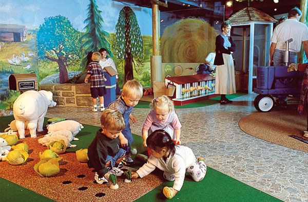 Toddlers playing in a vegetable garden mural, picking turnips and cabbages, with a pig and her piglets nearby.