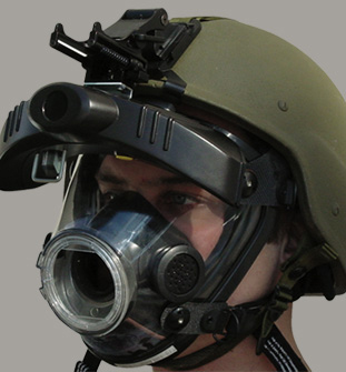 Helmet-mounted infrared night vision unit in matte black, staged with a gas mask to simulate use in hazardous environments.